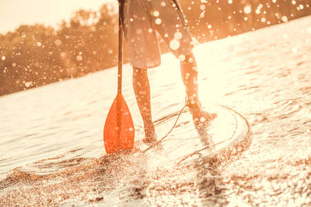 Cropped image of handsome young man SUP surfing on the river, sun is going downの写真素材