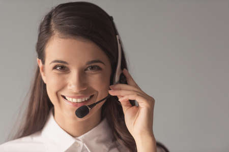 Beautiful young woman in headset is looking at camera and smiling, on gray backgroundの写真素材
