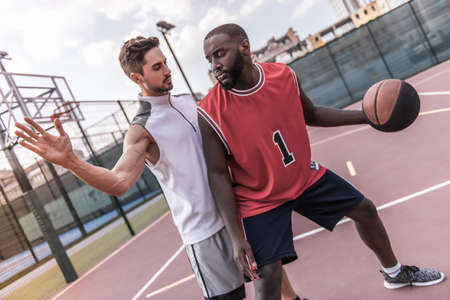 Handsome basketball players are playing on basketball court outdoorsの写真素材