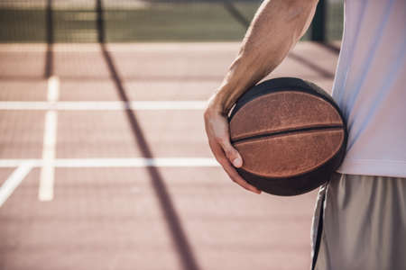Cropped image of basketball player holding a ball while standing on basketball court outdoorsの写真素材