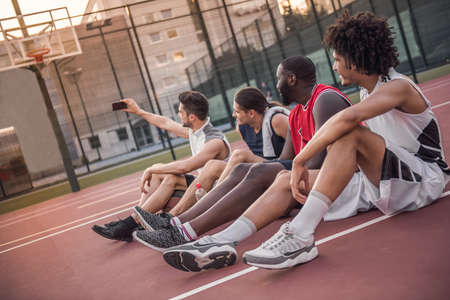 Handsome basketball players are talking and smiling while sitting on basketball court outdoors after the gameの写真素材
