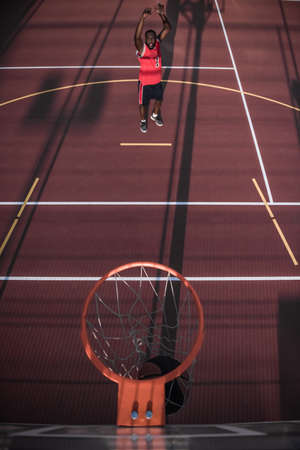 Top view of handsome Afro American basketball player shooting a ball through the hoop while playing on basketball court outdoorsの写真素材