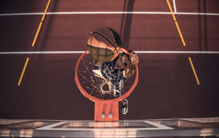 Top view of handsome basketball player shooting a ball through the hoop while playing on basketball court outdoorsの写真素材