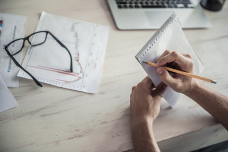 Cropped image of handsome young businessman in formal clothes making notes while working in officeの写真素材