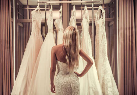 Back view of attractive young bride choosing wedding dress in modern wedding salonの写真素材
