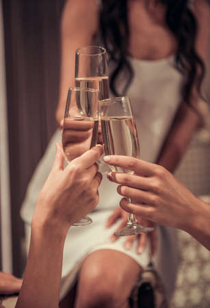 Cropped image of bride in elegant wedding dress and her friends clinking glasses of champagne while visiting modern wedding salonの写真素材