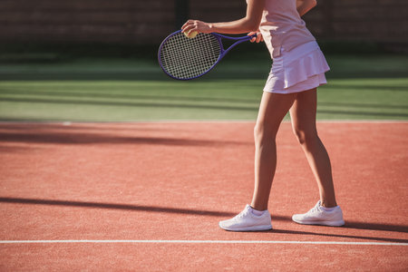 Cropped image of girl holding tennis racket while playing tennis on court outdoorsの写真素材