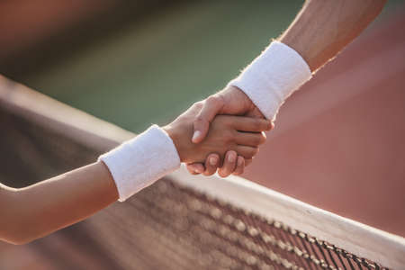 Cropped image of man and woman shaking their hands while playing tennis on tennis court outdoorsの写真素材