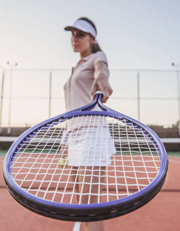 Beautiful young woman is posing with tennis racket while playing tennis on tennis court outdoorsの写真素材