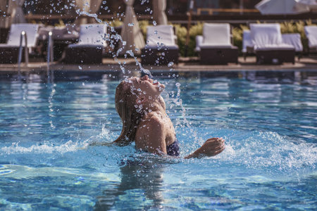 Beautiful girl in blue swimsuit is throwing her wet hair back while swimming in the pool
