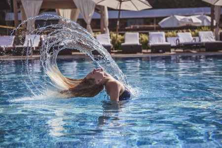 Beautiful girl in blue swimsuit is throwing her wet hair back while swimming in the poolの写真素材