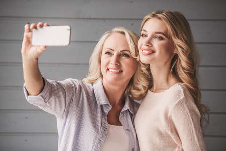 Beautiful senior mom and her adult daughter are doing selfie using a smart phone and smilingの写真素材