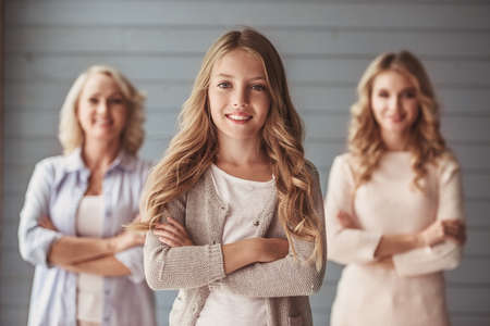 Beautiful women generation: granny, mom and daughter are looking at camera and smiling while standing with crossed arms, girl in the foregroundの写真素材