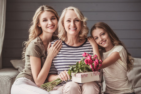 Beautiful women generation: granny with presents, mom and daughter are hugging, looking at camera...