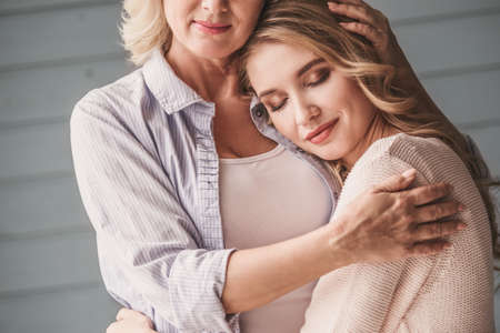 Beautiful senior mom and her adult daughter are hugging and smilingの写真素材