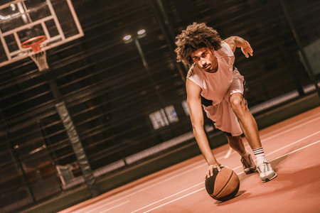 Attractive mulatto basketball player is playing basketball outdoors in the eveningの写真素材