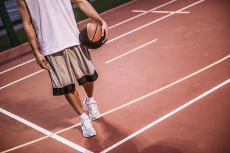 Cropped image of handsome basketball player standing with a ball on basketball court outdoorsの写真素材
