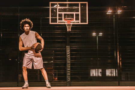 Attractive mulatto basketball player is playing basketball outdoors in the evening