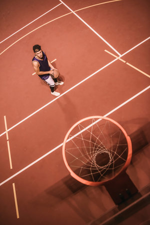 Top view of stylish young basketball player in cap shooting a ball through the hoop while playing outdoors at nightの写真素材