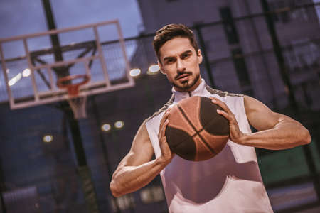 Handsome basketball player is playing basketball outdoors in the eveningの写真素材