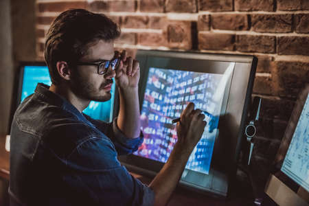 Handsome young programmer in casual clothes is working with computersの写真素材