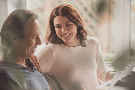 Beautiful couple is using a laptop, studying documents and smiling while working on couch at homeの写真素材
