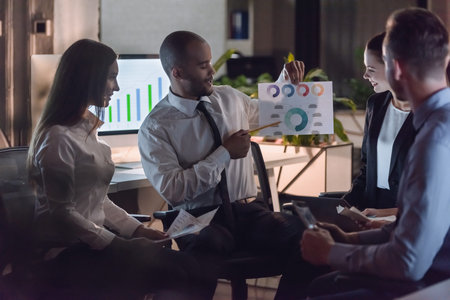 Successful business people are sitting in circle and discussing affairs while working in office late...