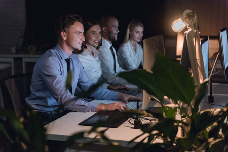 Successful business people in headsets are using computers and smiling while working in office late at nightの写真素材