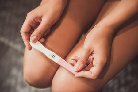 Cropped image of woman holding a pregnancy test on her kneesの写真素材