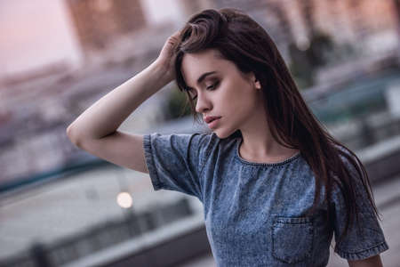 Portrait of beautiful dark-haired girl in jean dress on the city backgroundの写真素材