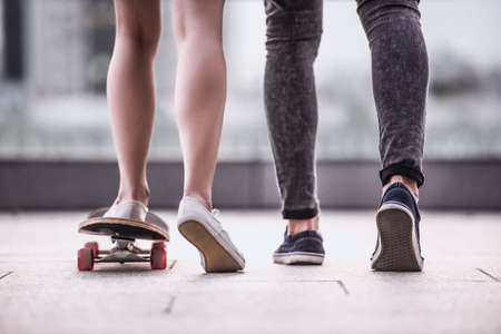 Cropped image of stylish young couple spending time together in the city. Guy is teaching his girl skateboardingの写真素材