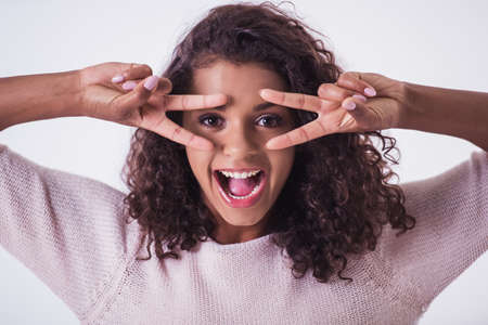 Beautiful Afro American girl is gesturing, looking at camera and smiling, isolated on white backgroundの写真素材