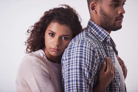 Beautiful Afro American girl is hugging her handsome guy and looking sadly at camera, isolated on whiteの写真素材