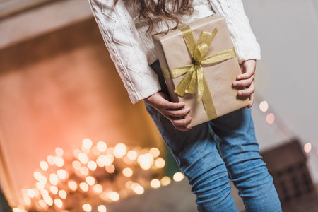 Merry Christmas and Happy New Year! Cropped image of little girl holding a present while standing in decorated roomの写真素材