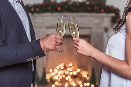 Merry Christmas and Happy New Year! Cropped image of elegant couple clinking glasses of champagne together while celebratingの写真素材