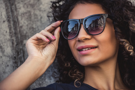 Portrait of attractive girl in sun glasses looking away and smiling, on concrete wall backgroundの写真素材