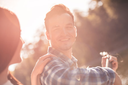 Beautiful young couple is singing and smiling while resting on a plaid in the park, guy is playing guitarの写真素材