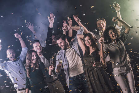 Happy group of people drinking champagne, dancing and smiling while celebrating New Year, on dark smoky backgroundの写真素材