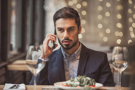 Handsome businessman in suit is talking on the mobile phone while sitting in restaurantの写真素材
