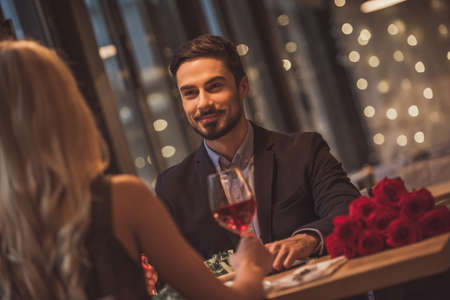 Handsome elegant man is looking at his girlfriend and smiling while they having a date in restaurantの写真素材