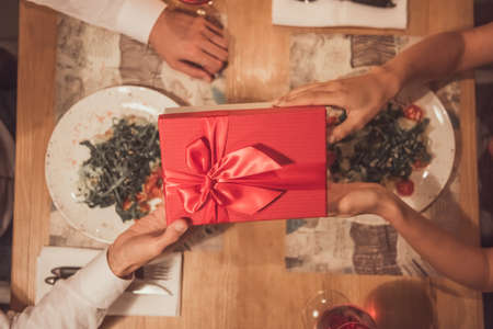 Cropped image of young couple holding a gift box while celebrating New Year in a restaurant, top viewの写真素材