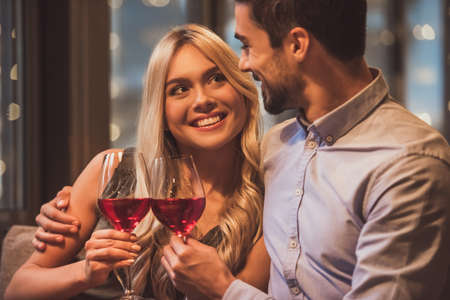 Beautiful young couple is looking at each other, drinking wine and smiling during their date in a restaurantの写真素材
