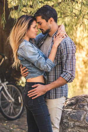 Beautiful young couple is hugging while resting in the park, a bicycle in the backgroundの写真素材