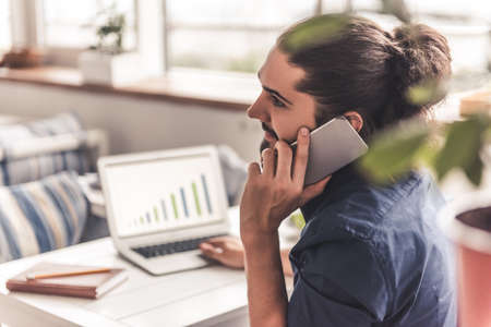 Handsome young businessman with long dark hair is talking on the mobile phone while working in the cafeの写真素材