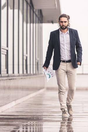 Full length portrait of handsome businessman holding document while walking outdoorsの写真素材