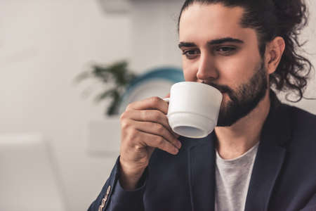Handsome young businessman with long dark hair is drinking coffeeの写真素材