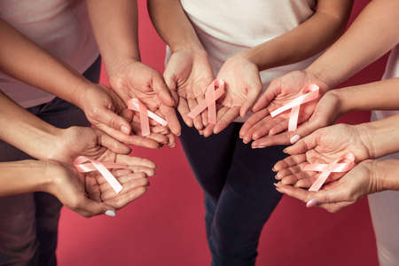 Women against breast cancer. Cropped image of woman holding pink ribbons in their palms, on red backgroundの写真素材