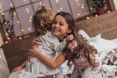 It's Christmas time! Cute little girls are hugging and smiling while spending time together in bed...