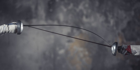Cropped image of weapon holding by female fencers while fighting on dark gray background