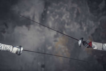 Cropped image of weapon holding by female fencers while fighting on dark gray backgroundの写真素材